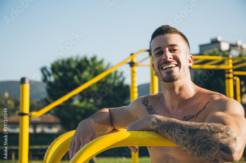 Portrait of a happy urban athlete with tattoos at the calisthenics gym