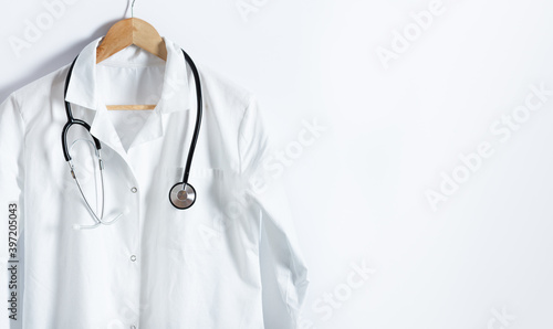 Doctor's white coat with stethoscope on hanger over white background with copy space.