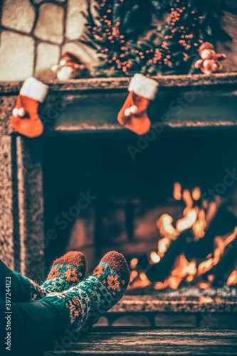 Feet in woollen socks by the fireplace. Woman relaxes by warm fire and warming up her feet in woollen socks. Close up on feet. Winter and Christmas holidays concept.