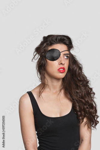 Thoughtful young woman wearing eye patch over gray background
