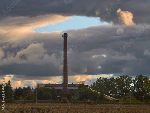 Komin fabryczny i otwarte czyste niebo nad nim, wokół same chmury i smog.