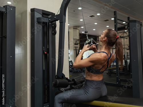 Athletic muscular woman exercising her back in lat exercise machine with narrow grip in the gym