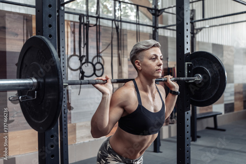 Portrait of a young muscular woman athlete with a barbell on her shoulders in a modern cross gym. Sport, fitness concept