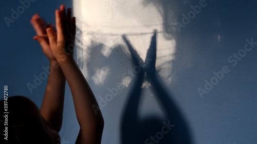 Child claps hands on unfocused foreground and focus to blurry hand shadows on wall background. Game with light and shadow. Dark spooky silhouettes of hands for Halloween concept