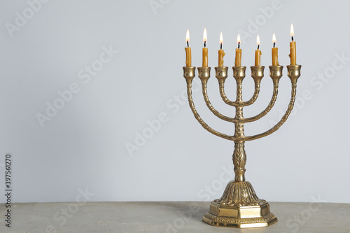 Golden menorah with burning candles on table against light grey background, space for text