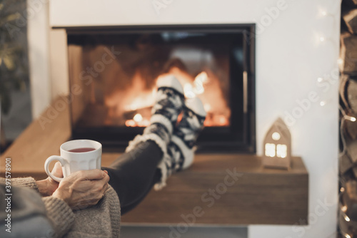 Woman relaxing near the fireplace, holding cup of tea, enjoying life at home. Winter fun, lifestyle, leisure, lockdown, holidays, vacations, Christmas, New Year concept