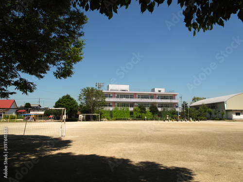 A wide view of a traditional multi-level Japanese school with exercise equipment and an empty yard in the foreground on a sunny day