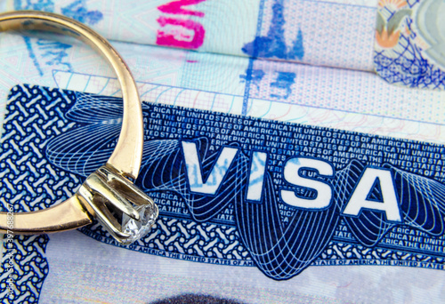 Engagement ring on top of blurred US entry visa sticker in a passport. Conceptual photo for fiance visa and immigration in general. Selective focus.