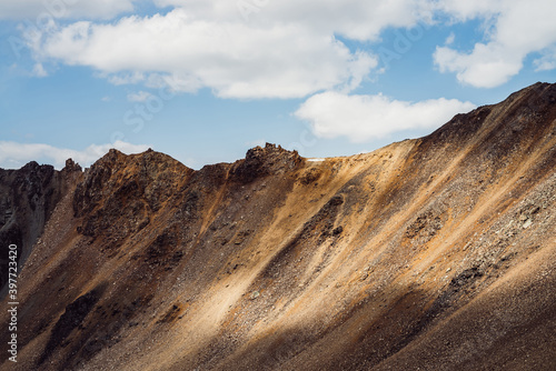 Atmospheric landscape with rocky mountain wall with pointy top in sunny gold light. Beautiful golden rock pinnacle in sunlight. Awesome mountain scenery with pointed rockies. Sharp stony mountains.