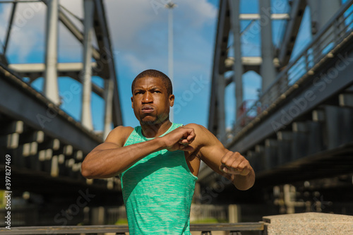 Waist up portrait of determined young Black athlete practicing arm warm up exercise before running training on urban bridge
