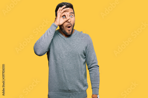 Handsome hispanic man wearing casual clothes doing ok gesture shocked with surprised face, eye looking through fingers. unbelieving expression.