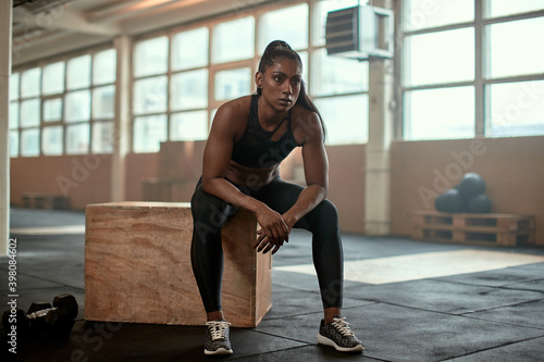 Serious ethnic female athlete resting near dumbbells