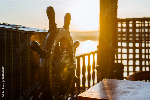 Wooden Helm or steering wheel of a shipping vessel with a sunrise in the background. Indicative of journey and transportation