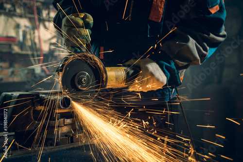 Locksmith in special clothes and goggles works in production. Metal processing with angle grinder. Sparks in metalworking