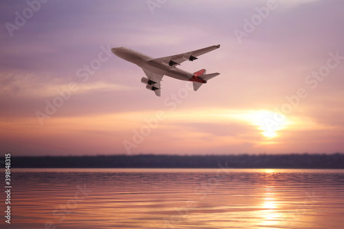 Modern airplane flying over river during sunset
