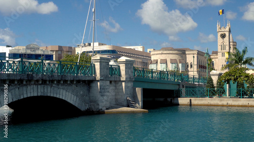 Bridgetown, Barbados: Chamberlain bridge with people passing and Parliament building with the flag on top of the tower in the background