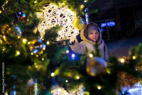 Dziewczyna dotyka ogromnej bombki wiszącej na kolorowo oświetlonej miejskiej choince będącej ozdobą Świąt Bożego Narodzenia, Polska