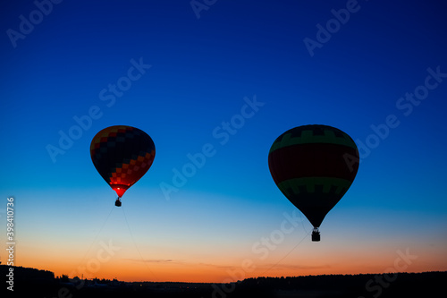 Two Colorful Air Balloons Levitating Over the Field Outdoors Against Clear Blue Skies At Twilight.