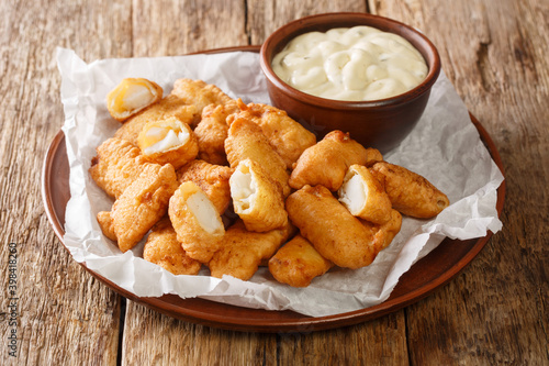 Fish appetizer consisting of deep-fried cod pieces and served with a dipping sauce closeup in the plate on the table. Horizontal