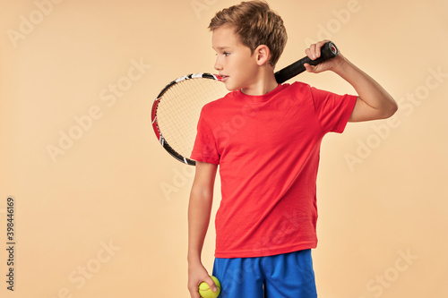 Cute boy tennis player standing against light orange background