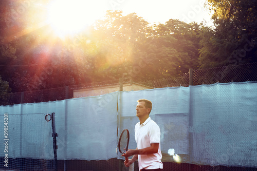 Young man plays tennis outdoors on tennis court in the morning
