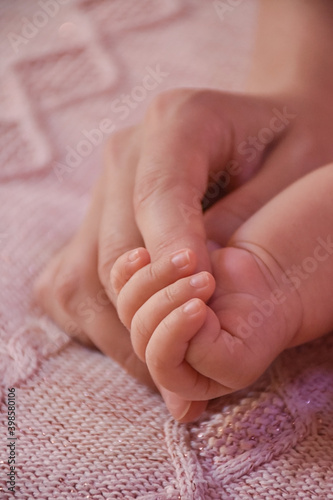 Newborn girl baby holding mother's finger on pink background. Concept of love and family relationship 