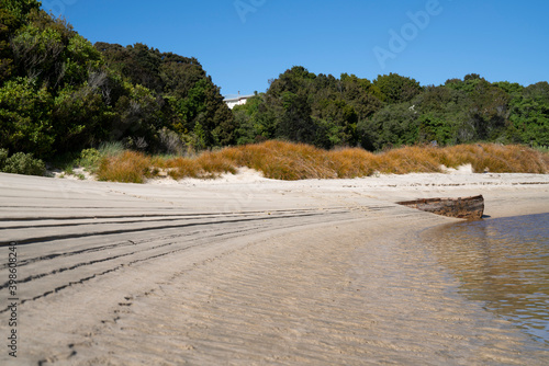 Lines and patterns curving along edge of stream interupted by bow of old wooden boat stuck in sand