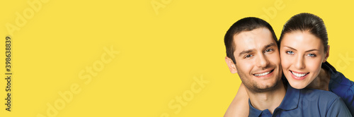 Love, relationship, lovers concept - studio portrait image of happy smiling embracing couple, man and woman in piggyback pose, isolated over yellow color background. Copy space for text.