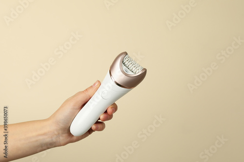 Female hand hold epilator on beige background, space for text