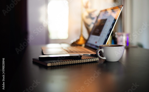 Close-up of white coffee cup and mobile phone put on book with blur computer laptop background, Vintage light and dark tone