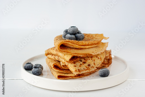 Vegan crepes made from chickpea flour, al purpose gluten free flour and oat milk, with frozen blueberries on a white wooden table