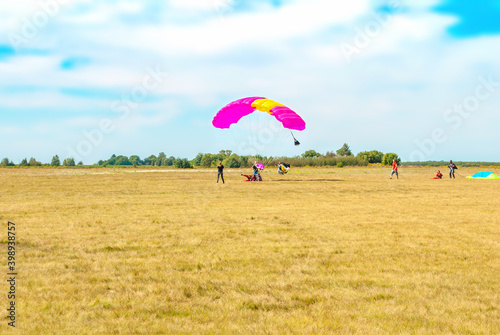 Paraglider landing on summer field by blue sky