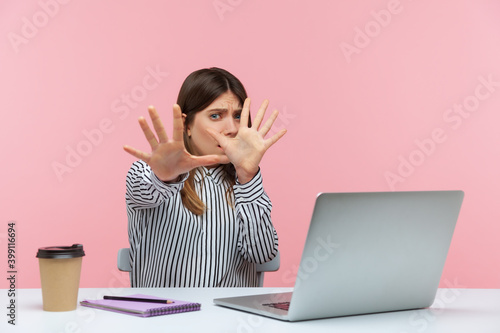 No, I'm scared! Frightened woman with shocked expression raising hands in stop gesture, defending herself, freaked out of troubles working on laptop. Indoor studio shot isolated on pink background
