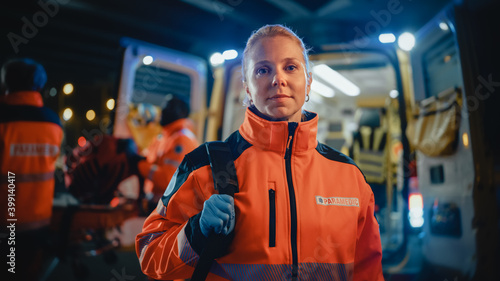Portrait of a Female EMS Paramedic Proudly Standing in Front of Camera in High Visibility Medical Orange Uniform with "Paramedic" Text Logo. Successful Emergency Medical Technician or Doctor at Work.