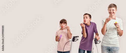 Three cheerful disabled children with Down syndrome and cerebral palsy smiling while blowing soap bubbles, standing together isolated over white background