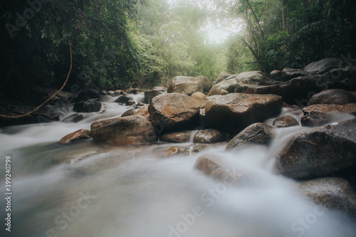 Beautiful waterfall stream in tropical rainforest scenery in the morning in slow shutter mode.Selective focus shot.Image contain grain due to slow shutter shot.