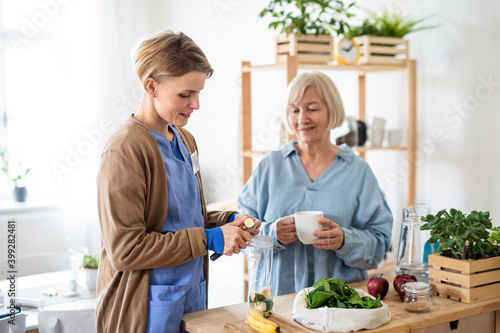 Senior woman with caregiver or healthcare worker indoors, preparing food.