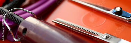 Close up of professional hairdressing scissors, hair clipper and hairgrips on red surface