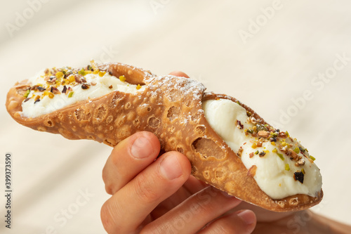 Close up of a fresh Sicilian Cannoli, held by hand. .