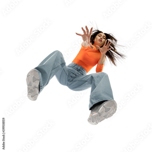 Dancing. Young stylish woman in modern street style outfit isolated on white background, shot from the bottom. West fashionable model in sneakers and sweetshirt, musician, rapper performing.