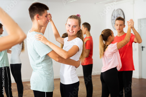 Group of teenage boys and girls training movements of slow foxtrot in dance studio with female coach