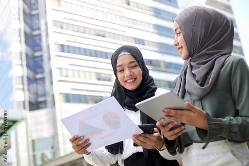 Two young Asian Muslim businesswomen stand together in a central business district.