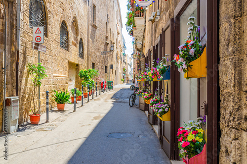 Narrow cobblestone street in Taranto historical city center. Typical italian street with flowers in pots, bicycle and stone walls of buildings in sunny day, Puglia Apulia, Italy