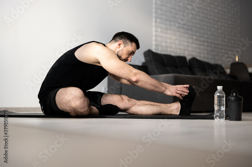 Stretch body exercise. Yoga position. Man stretching before workout. Black sportswear. Athletic man warming up on black yoga mat. Sports during quarantine. Remember to warm up before hard workout.