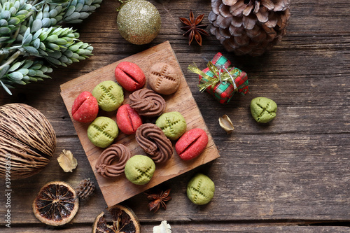 homemade colorful chocolate, green tea and coffee cookies are on the small wooden slats with chritmas ornaments decoration , cinnamon, pinecone, star anise and chritmas ornament on the wooden table