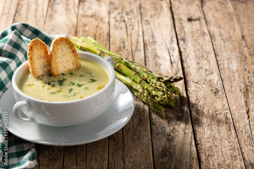 Fresh green asparagus soup in bowl on wooden table. Copy space