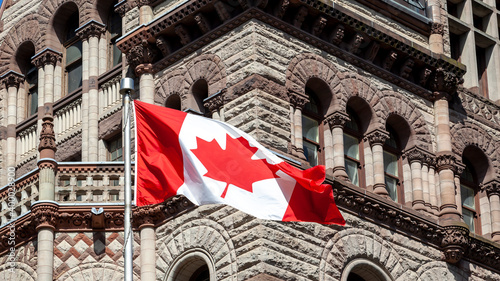 The waving Canadian flag with Old City Hall in background in Toronto, Canada. Toronto is the provincial capital of Ontario and the most populous city in Canada.