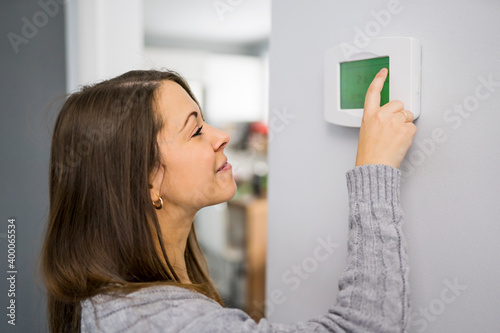 Woman set the thermostat at house.