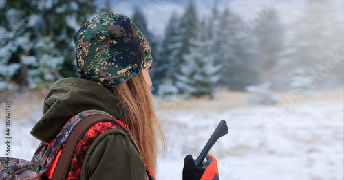 A young beautiful hunter woman on hunt in forest with rifle on the shoulder. Winter season.