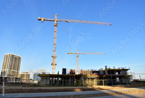 Tower cranes working at construction site on blue sky background. Construction process of the new modern residential buildings